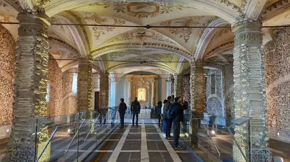 Visitors walking through the arched interior of the Chapel of Bones in Évora