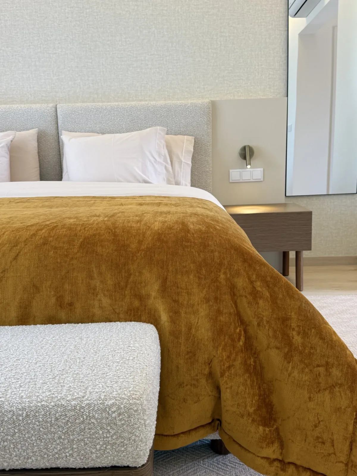 Cama de casal com uma manta de veludo mostarda e um banco estofado