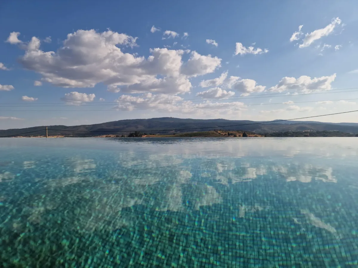 Piscina infinita que reflete o céu, com a Serra d'Ossa no horizonte