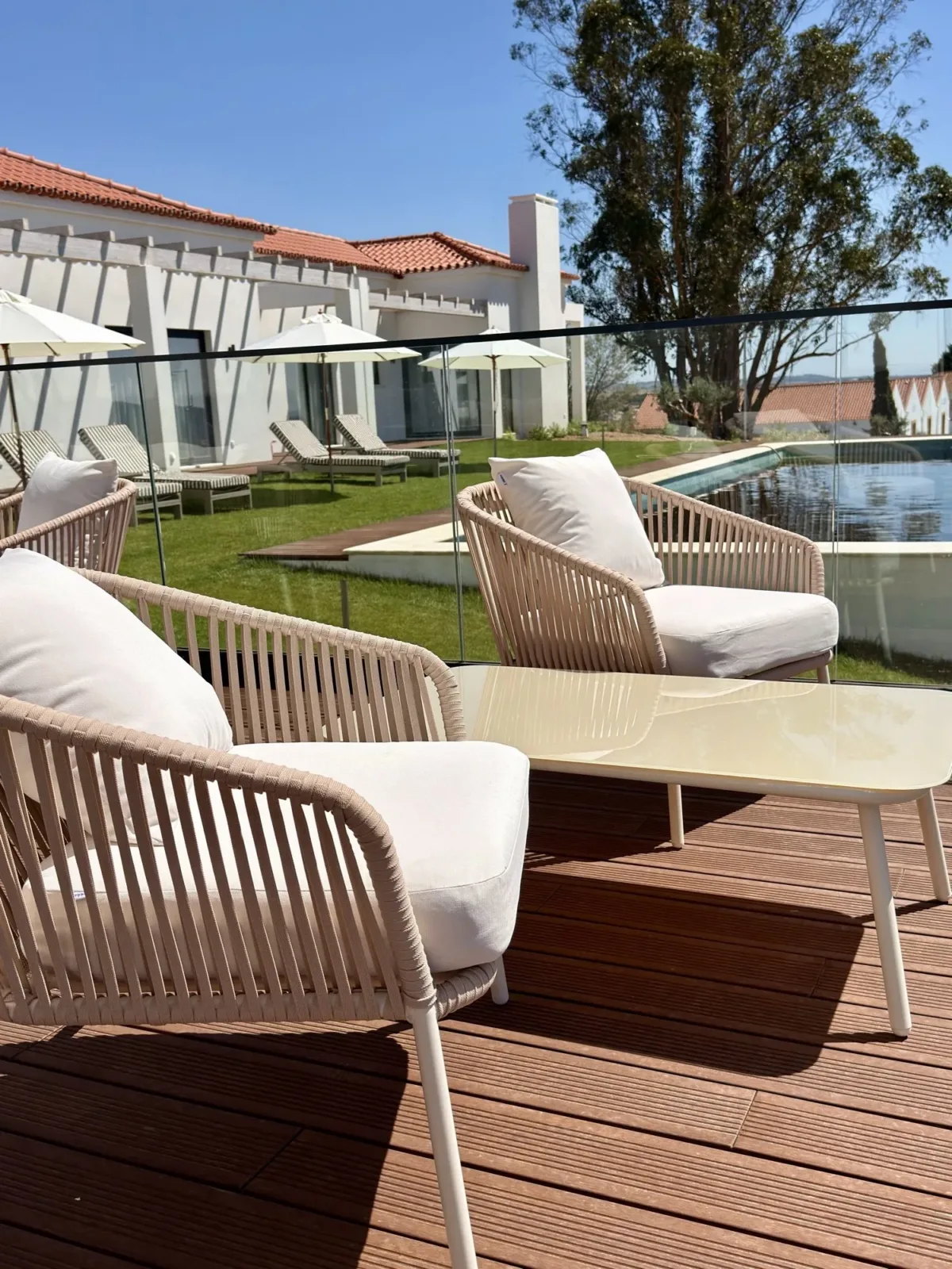 Cadeirões de vime no terraço, com a piscina e o relvado ao fundo